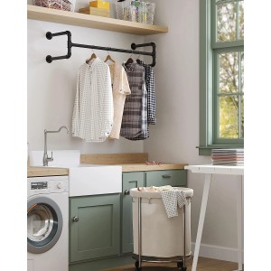 Schwarze Songmics Kleiderstange zur Wandbefestigung mit Kleidung im Raum.