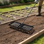 Schwarzer Relaxdays Rasenrakel aus Stahl mit langem Stiel, wird zum Ebnen von Erde in einem Gartenbeet genutzt.