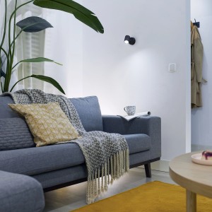 Schwarze WIZ LED Deckenleuchte Imageo Spot im Wohnzimmer mit Sofa und Pflanze.