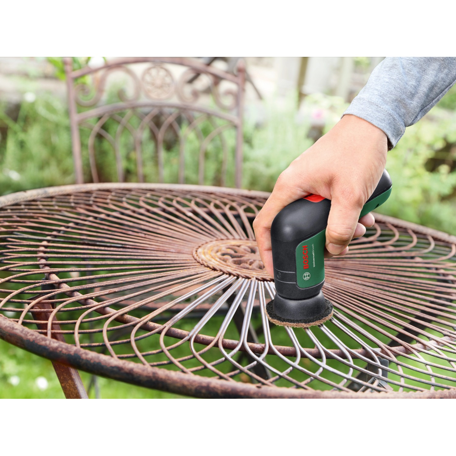 Bosch Akku-Bürste Universal Brush im Einsatz zum Reinigen eines Gartentisches.