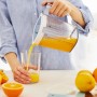Frau gießt Saft aus transparentem Rotho Messbecher in ein Glas. Küchenhelfer mit Skala.