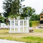Axi Spielhaus Max mit Rutsche und Leiter im Garten, im Hintergrund eine DIY-Bar aus Paletten.