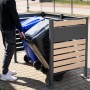Westmann Mülltonnenverkleidung Planum für 2 Tonnen (240 l) in Holzoptik. Person schiebt Mülltonne in die Box.