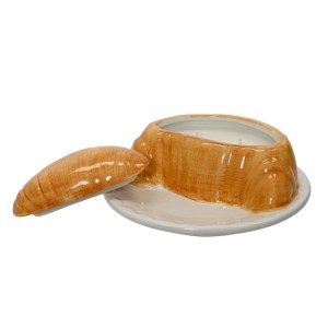 Braune Duftkerze in Croissantform mit glasiertem Finish, Deckel und Wachs auf weißem Teller.