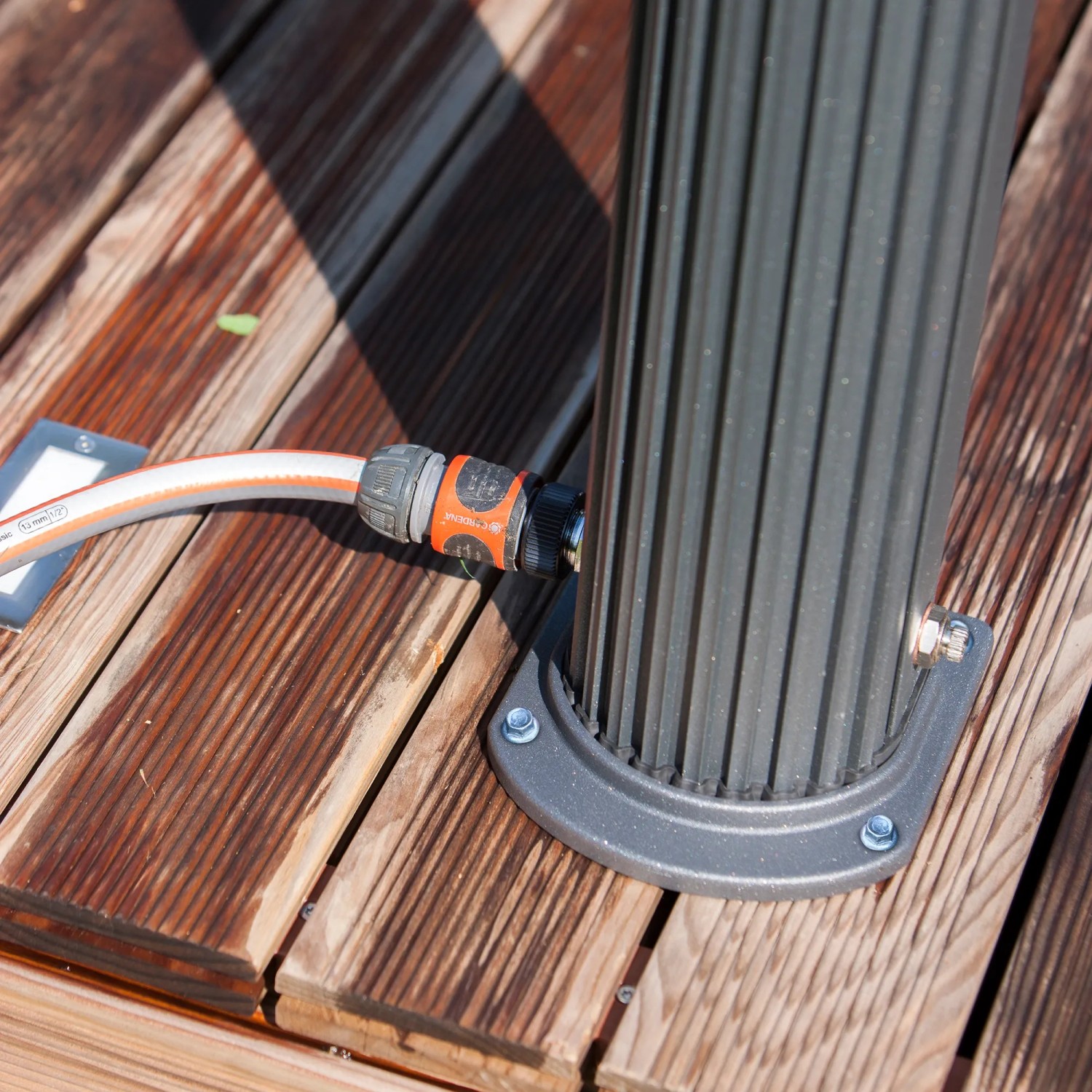 Detailaufnahme: Schwarze Gre Solardusche aus Aluminium mit Gartenschlauchanschluss auf Holzterrasse.