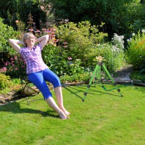 Relaxdays Kreisregner auf Stativ im Garten mit entspannter Frau im Hintergrund.
