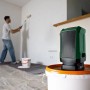 Grüner Bosch Akku-Bluetooth-Box UniversalSpeaker 18V-1 auf Eimer, Mann streicht Wand.