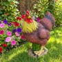 Dekorative Gartenfigur Hahn aus Polyresin, braun mit gelbem Hals und rotem Kamm, steht im Gras vor bunten Blumen.