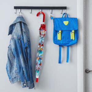 Transparenter Kinder-Regenschirm mit bunten Autos und rotem Griff, hängt an Garderobe neben Jacke und Rucksack.