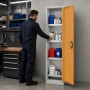 Grau-gelber JAN NOWAK Sicherheitsschrank PETER, offen in Werkstatt. Mann lagert Chemikalien in Säulenschrank.