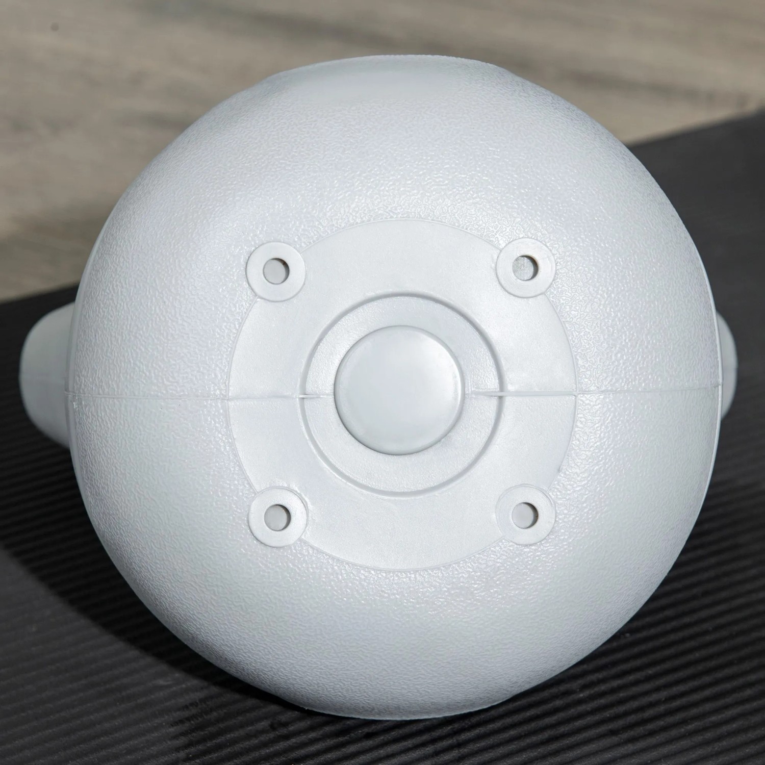 Unterseite einer hellen Kettlebell aus Kunststoff auf Fitnessmatte. Flacher Boden für sicheren Stand beim Gewichtstraining.