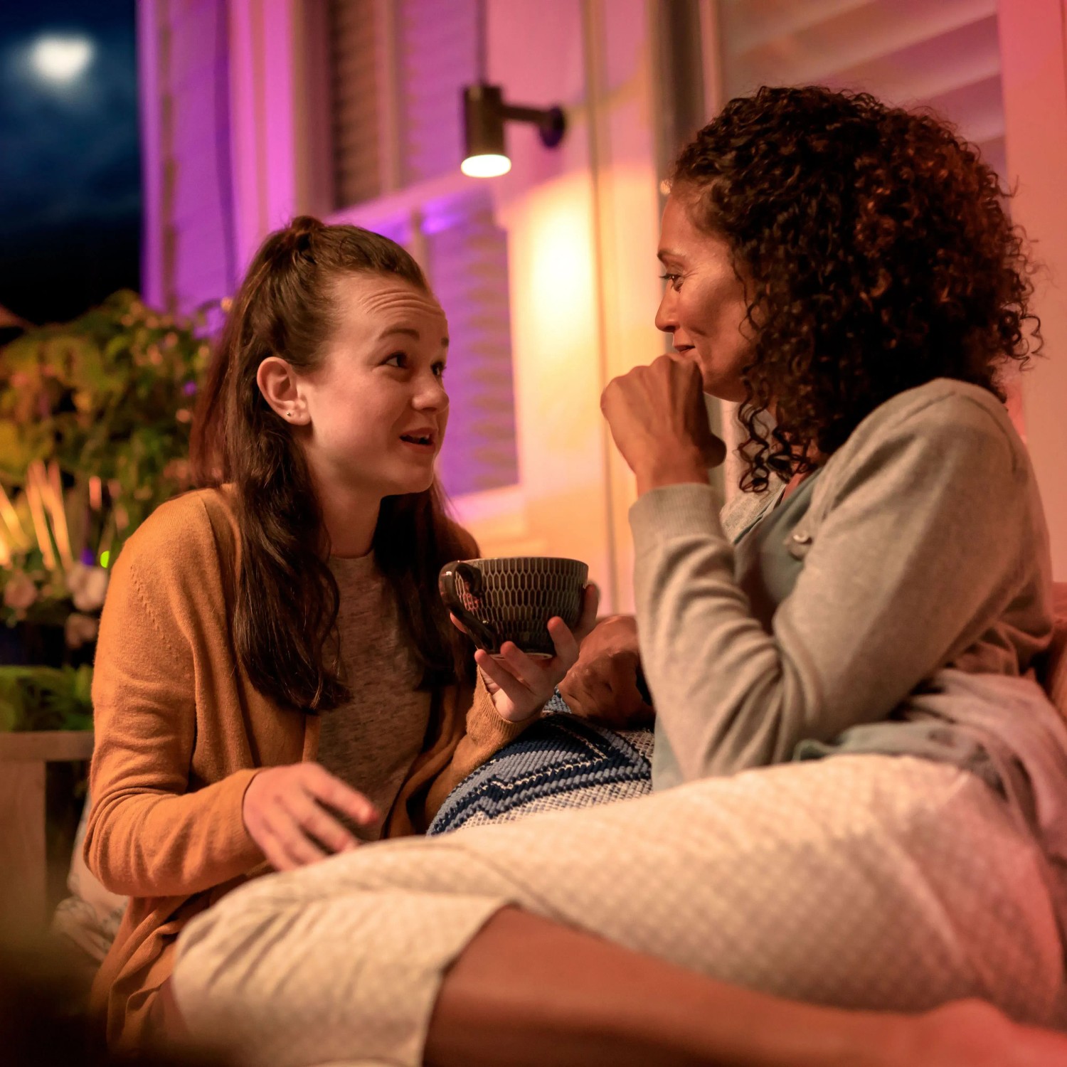 Zwei Frauen unterhalten sich im farbigen Licht der Philips Hue Lily Außenleuchte.