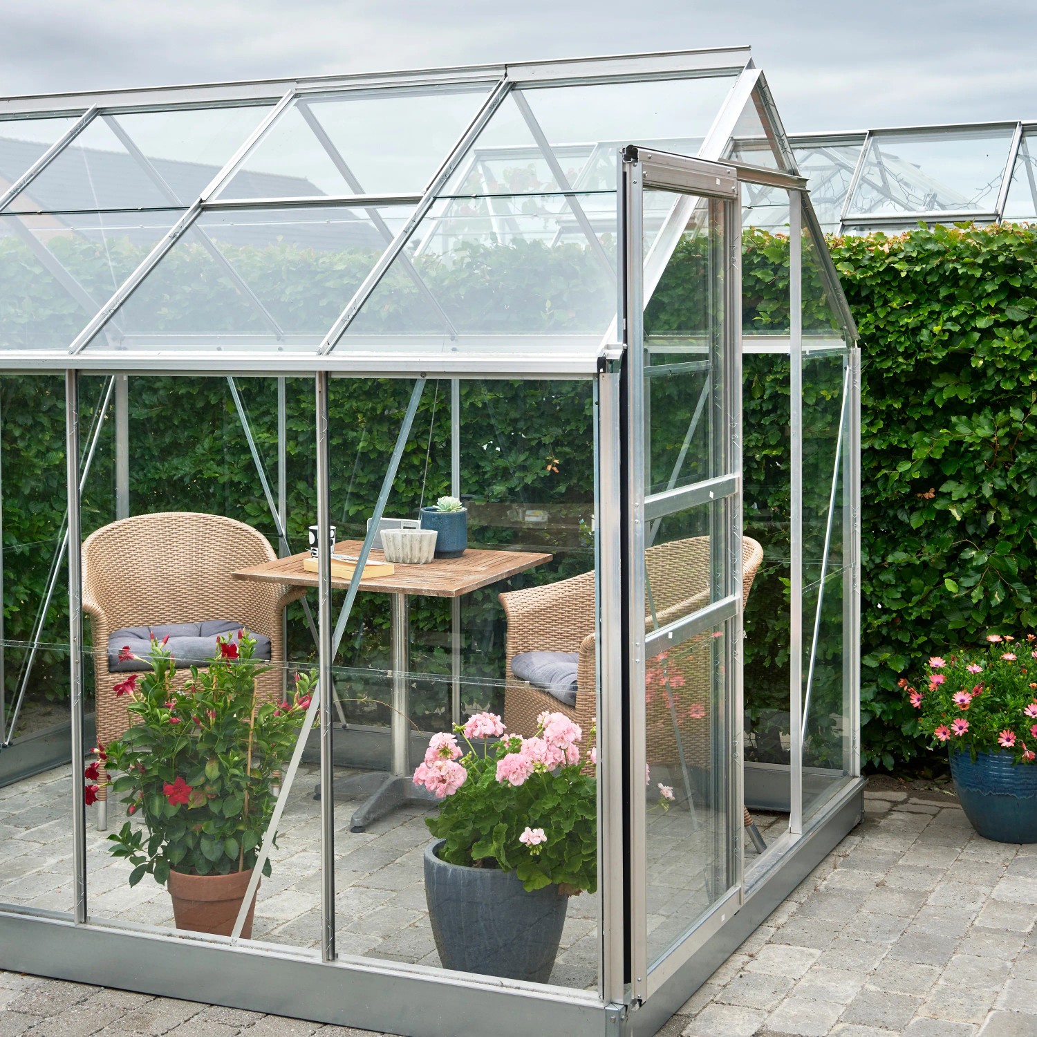 Halls Gewächshaus Popular 86 Alu, 5 m² mit Fundamentrahmen, eingerichtet mit Tisch und Stühlen.