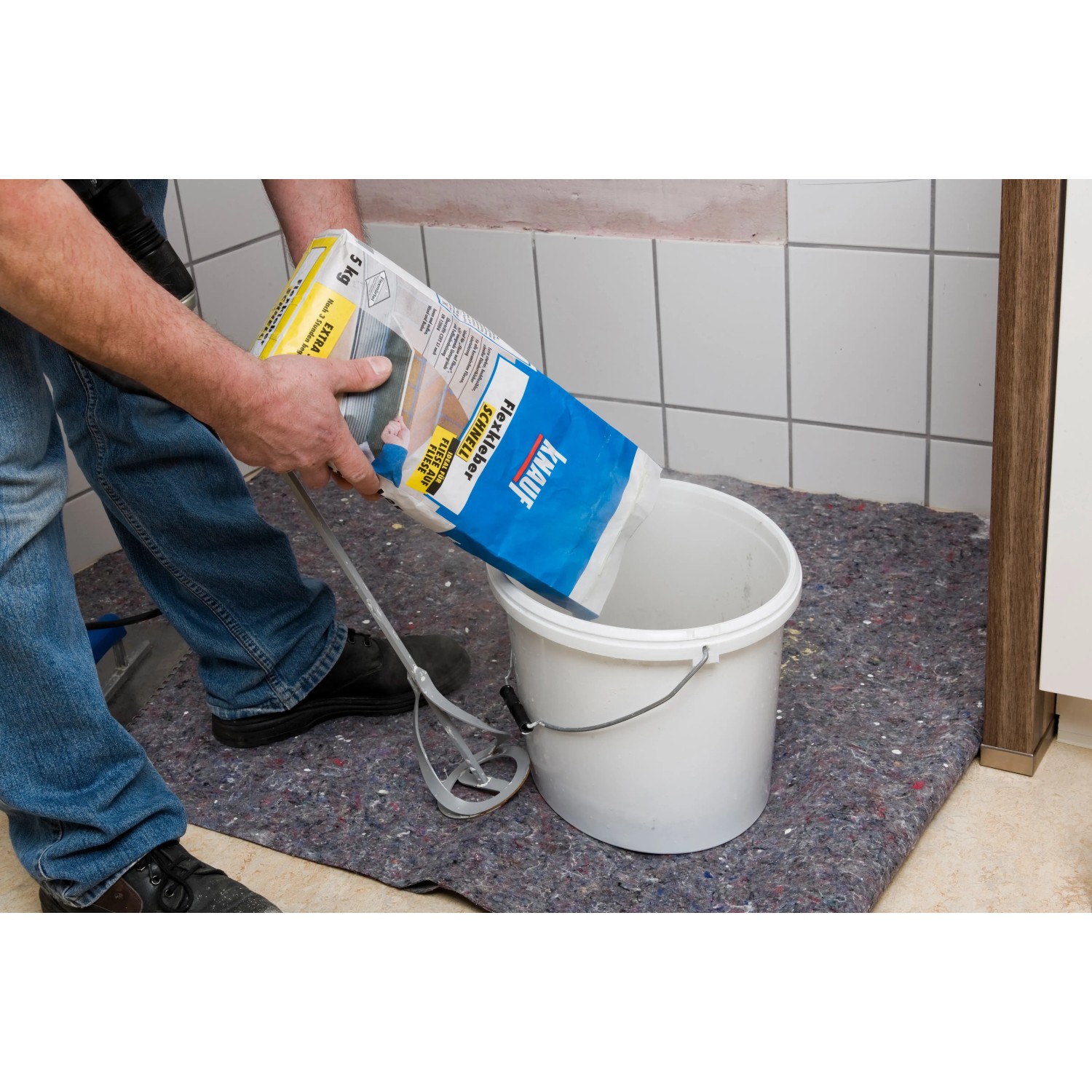 Knauf Flexkleber Schnell Grau wird in einen Eimer gefüllt.