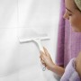 Frau benutzt Leifheit Duschabzieher Cabino an weißen Fliesen.