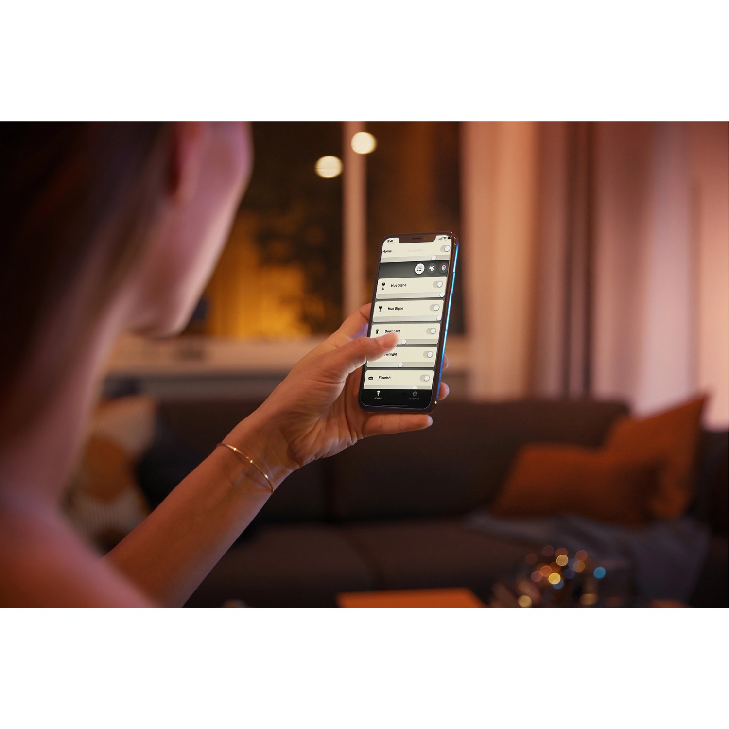 Frau steuert Philips Hue Leuchtmittel E27 per App. Warmweißes bis kaltweißes Licht.