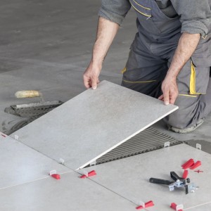 Fliesenleger verlegt graue Bodenfliesen mit Xpotool Nivelliersystem. Zuglaschen und Keile für 1,0mm Fugen sichern ebene Flächen.