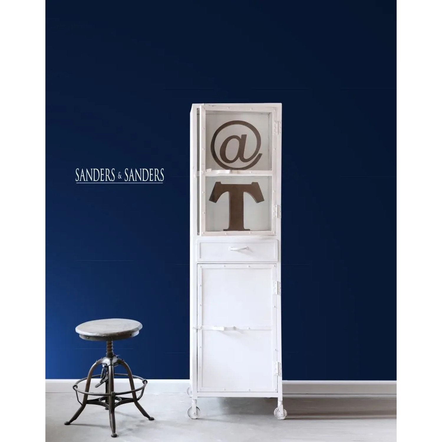 Sanders & Sanders Uni Vliestapete in Marineblau an einer Wand, davor ein weißer Schrank und Hocker. Moderne Wandgestaltung.