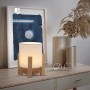Näve LED-Akkutischleuchte Madita mit Holzfuß und weißem Textilschirm auf Kommode.