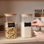 Transparente Vorratsgläser aus Glas mit Bambusdeckeln für Müsli & Reis auf Regal. Hand beschriftet Etikett.