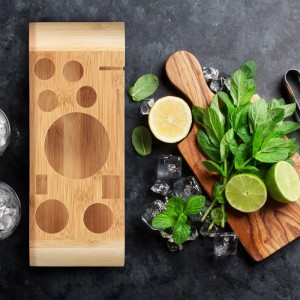 Bambus Ständer für Cocktailset mit Aussparungen, daneben frische Minze, Zitrone, Limette und Eiswürfel für Mixgetränke.