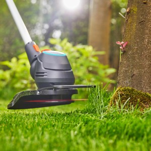 Gardena Akku-Trimmer ComfortCut 23/18V beim Rasenkantenschneiden nah am Baum.