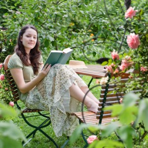 Frau liest Buch im Garten mit Rankgitter im Hintergrund. Entspannung im Grünen.