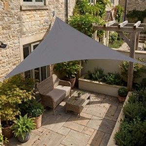 Anthrazitfarbenes, dreieckiges Sunula Sonnensegel aus Polyester über einer sonnigen Terrasse mit Gartenmöbeln.