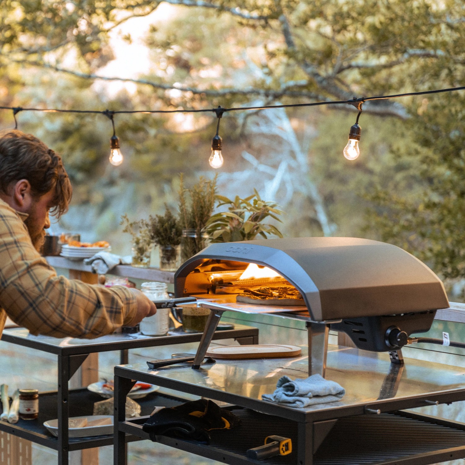 Ooni Koda 16 Gas Pizzaofen beim Pizzabacken im Garten unter Lichterkette.