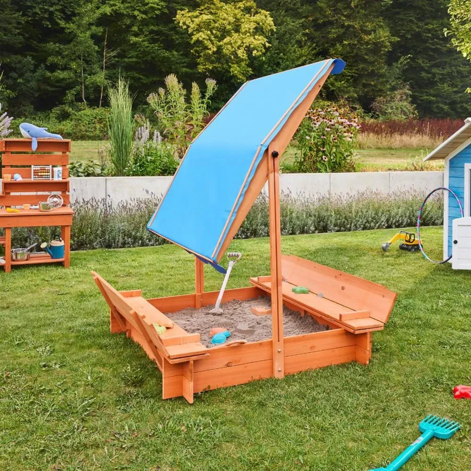 Home Deluxe Sandkasten Buddelkiste mit blauem Dach und Sitzbänken im Garten.