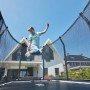 Schwarzes Salta Premium Ground Trampolin 305x214 cm mit springendem Kind vor Haus.