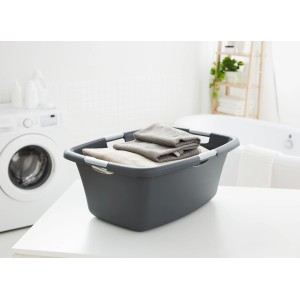 Anthrazitfarbene Rotho Wäschewanne Flowers (50 l) mit Wäsche vor Waschmaschine und Badewanne.