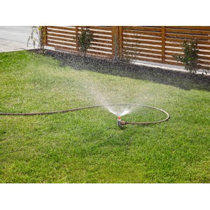 Gardena Sprühregner bewässert Rasenfläche. Regner mit Schlauch auf Grünfläche.
