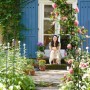 Dunkelgrüne Metall Torbogen Rankhilfe mit blühenden Rosen im Garten, eine Frau sitzt im Hintergrund.
