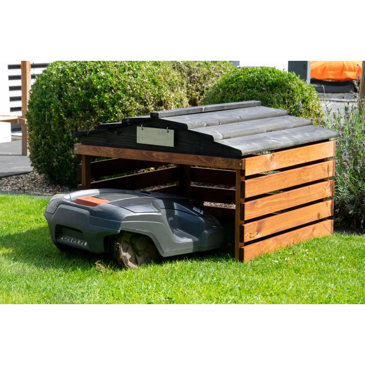 Dobar Mährobotergarage aus Holz, braun-schwarz, mit Mähroboter im Garten.