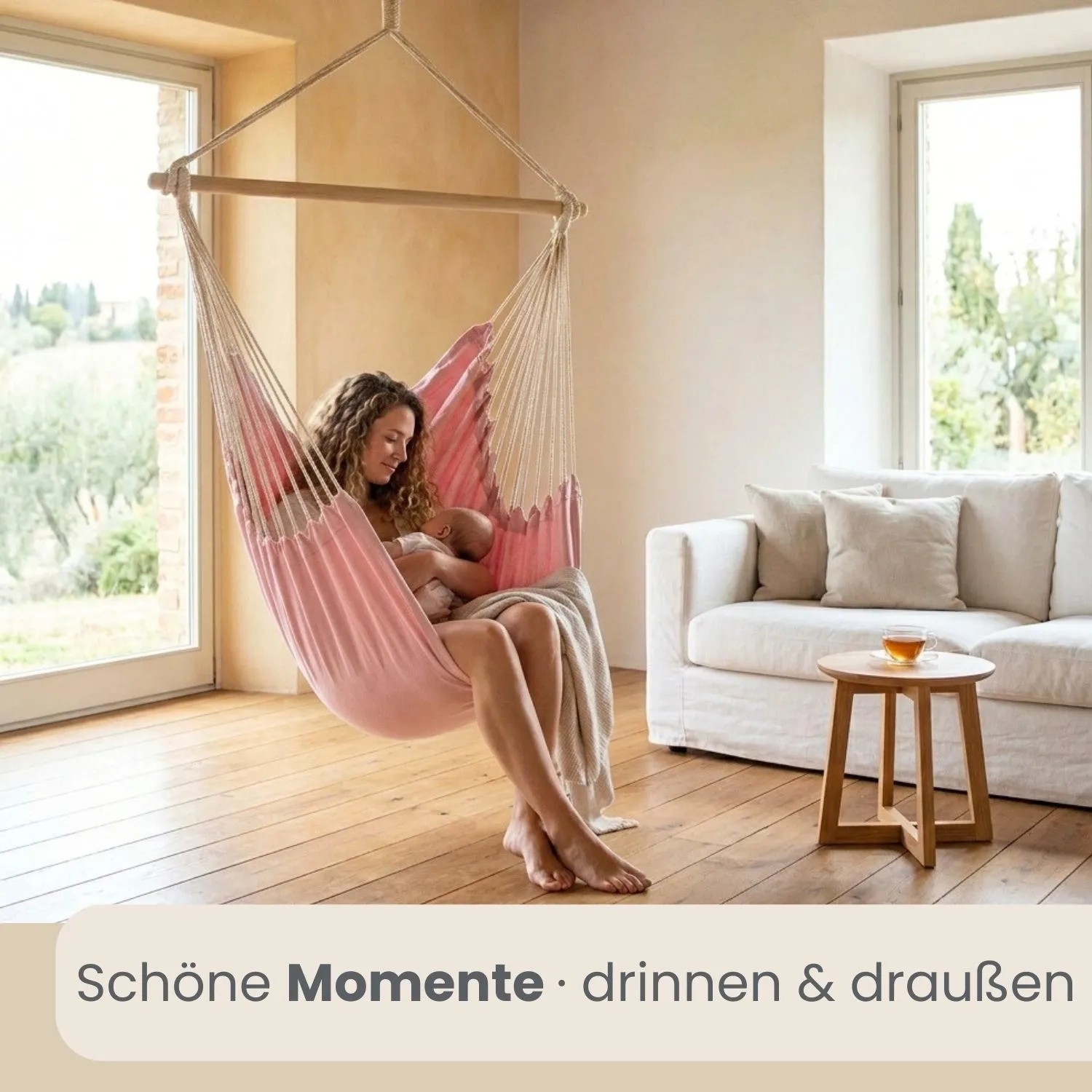 Rosa XXL Hängesessel mit Holzstab, Frau mit Baby entspannt im Wohnzimmer. Gemütlicher Schwebesessel für Indoor & Outdoor.