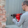 Mann bohrt mit rotem Einhell Bohrhammer TC-RH 900 in eine Ziegelwand.