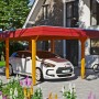 Skan Holz Carport Wendland Eiche hell mit roter Blende und Auto. Einzelcarport mit Flachdach.