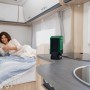 Dunkelgrüner Bosch UniversalSpeaker 18V-1 Akku-Bluetooth-Lautsprecher auf Arbeitsplatte im Wohnmobil. Frau liest im Bett.