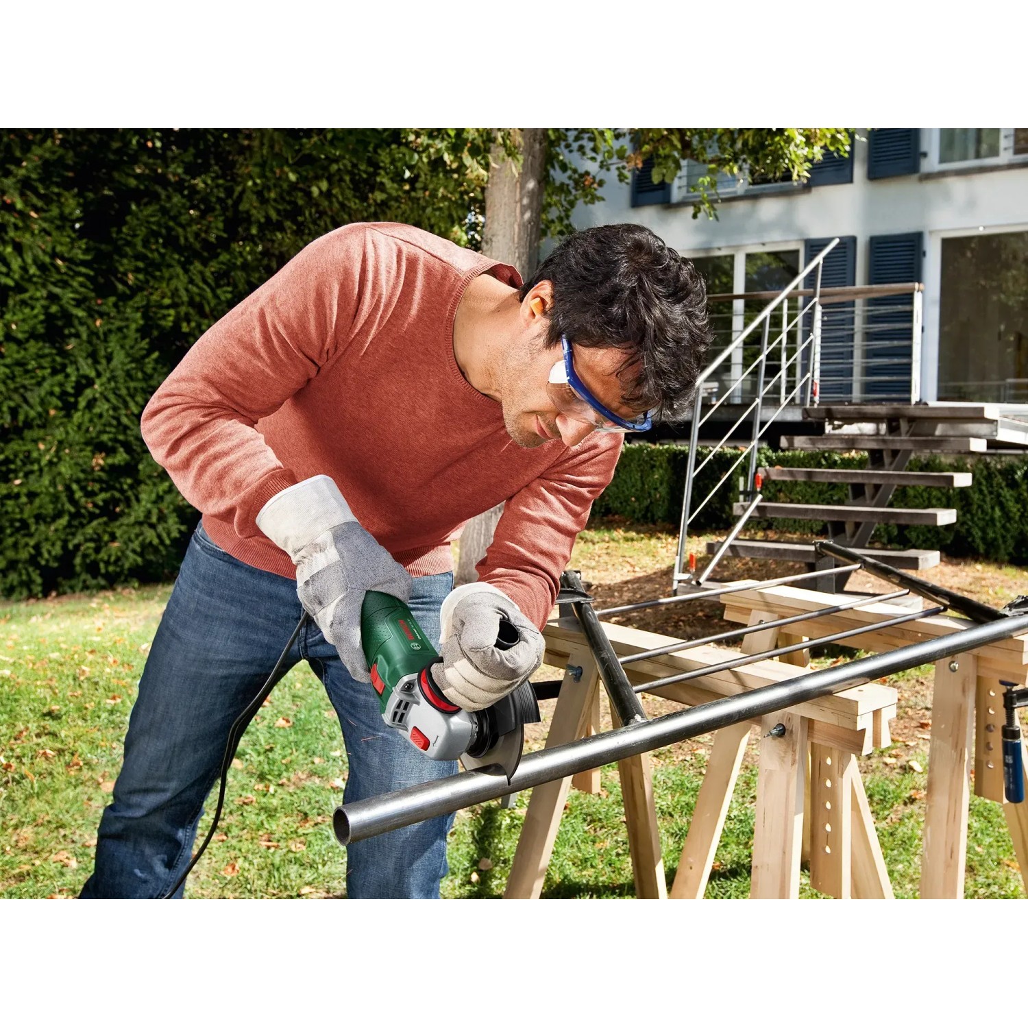 Mann schleift Metallrohr mit Bosch UniversalGrind 850-125 Winkelschleifer im Garten.