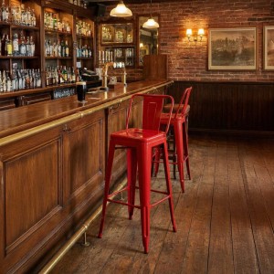 Rote DELUKE Barhocker LEKEL aus Metall vor einer Bar mit Tresen.