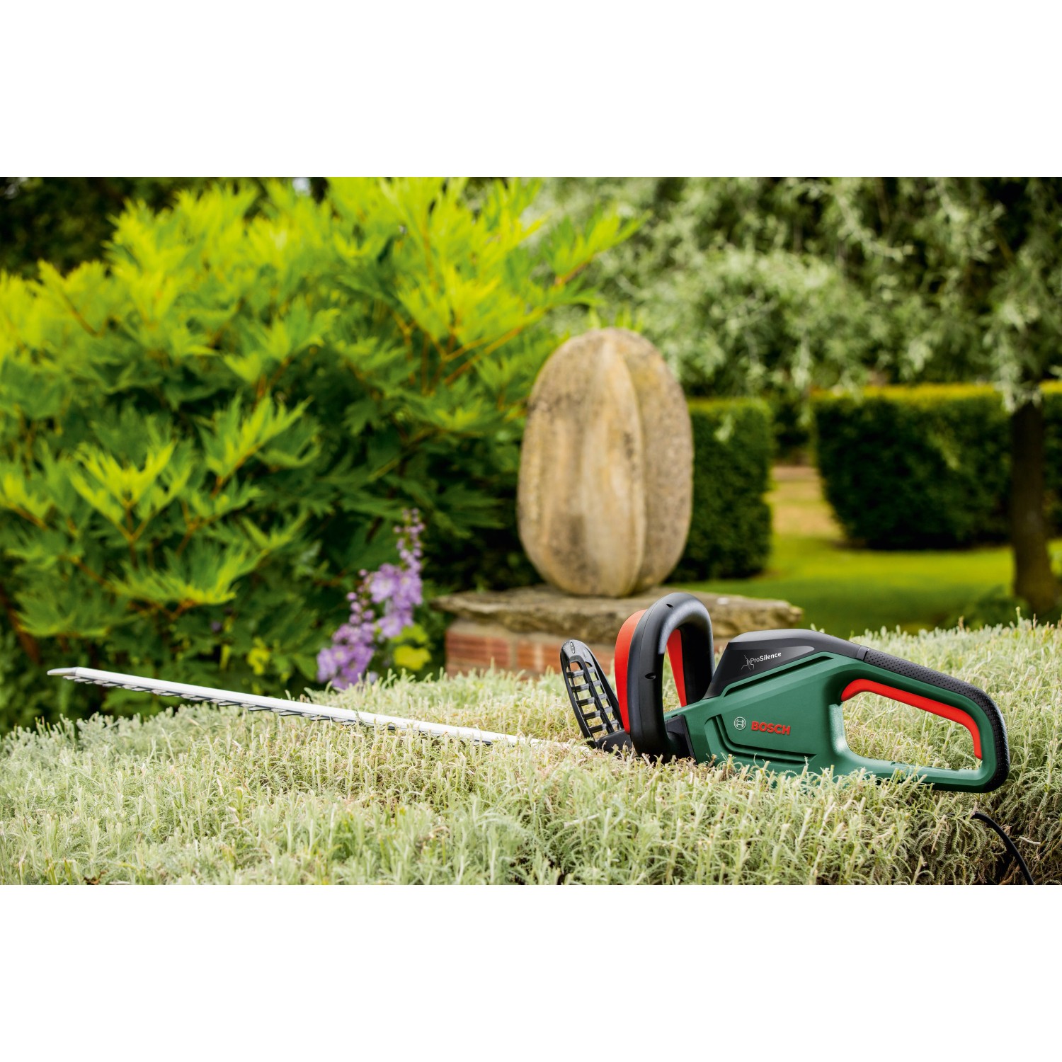 Bosch UniversalHedgeCut 60 Elektro-Heckenschere im Garten, grüne Hecke im Hintergrund.