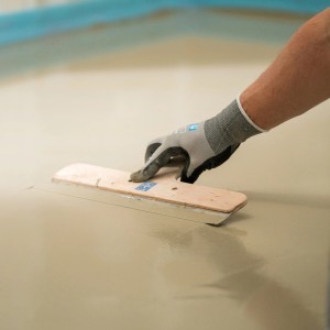 Handwerker verteilt Mapei Bodenausgleichsmasse (3-30 mm) mit einer Glättkelle auf dem Boden.
