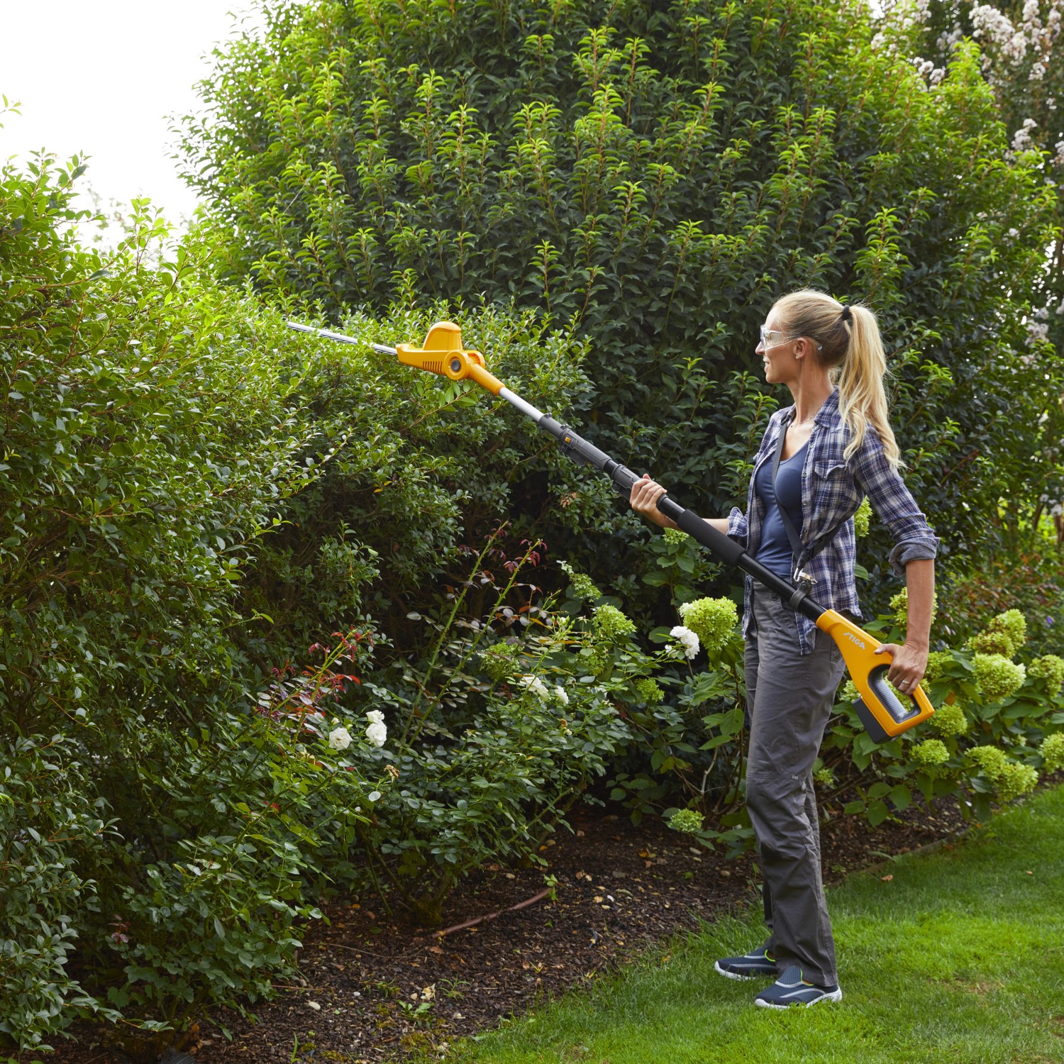 Frau schneidet Hecke mit Stiga Akku-Multitool MT 100e Heckenschere. Inkl. Akku und Ladegerät.