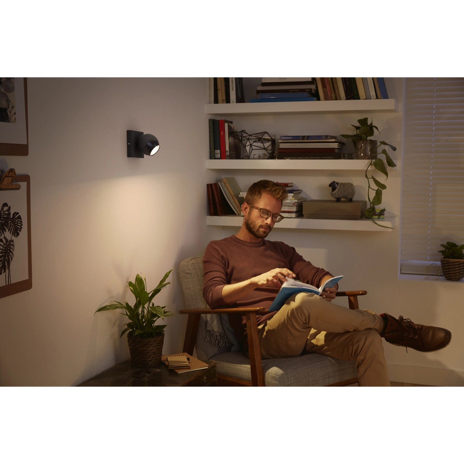Philips Hue Buckram Spot, schwarz, mit Mann beim Lesen im Sessel. Warmweißes Licht.