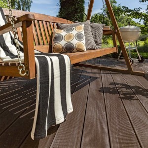 Dunkelbraune WPC Terrassendielen Samana auf Terrasse mit Gartenschaukel und Grill.