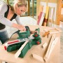 Frau sägt Holz mit Bosch Stichsäge PST 700 E. Kompakte 500W Säge für präzise Schnitte.