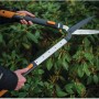 Fiskars SmartFit HS86 Teleskop-Heckenschere im Einsatz vor einer Hecke.