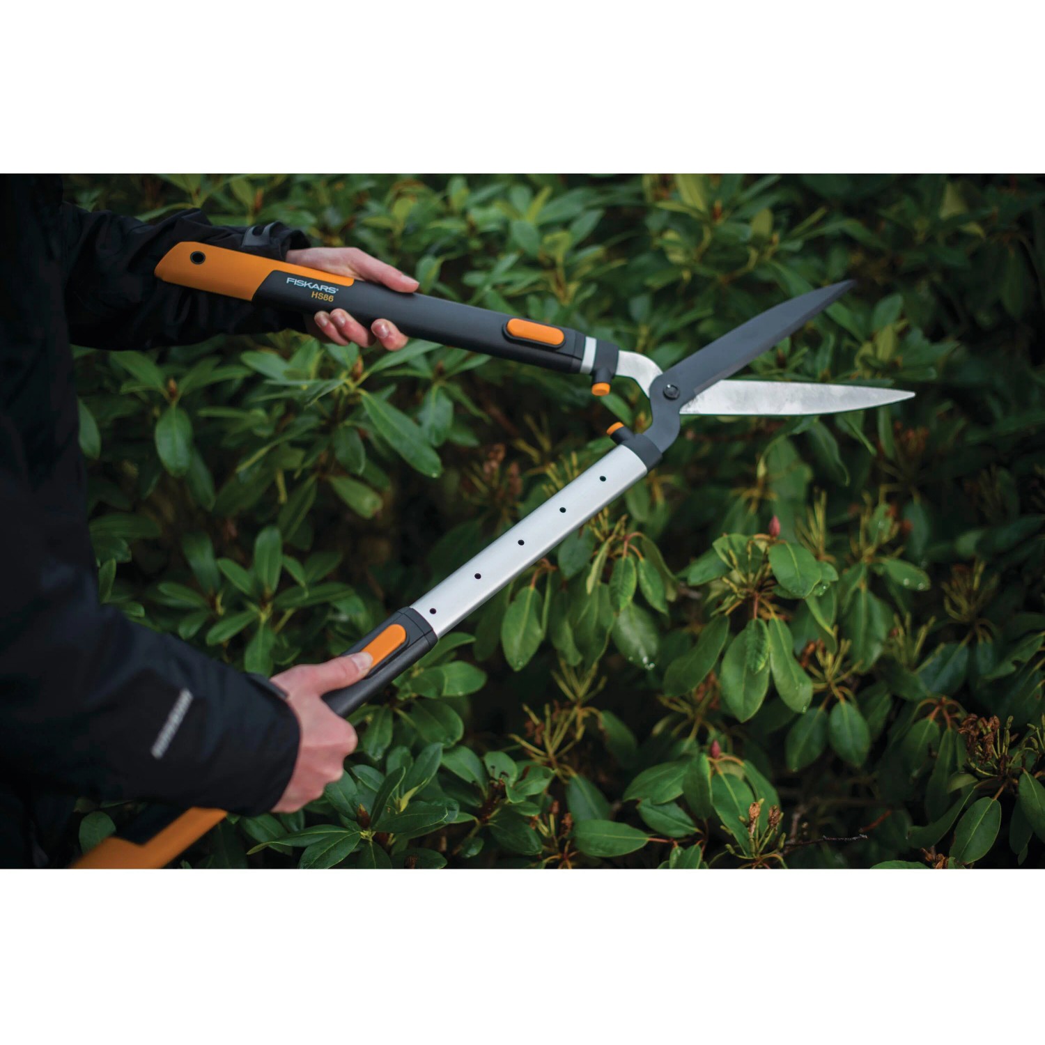 Fiskars SmartFit HS86 Teleskop-Heckenschere im Einsatz vor einer Hecke.
