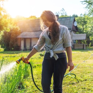 Frau bewässert Garten mit Schlauch. Im Vordergrund: Relaxdays Schlauchführung 5er Set.